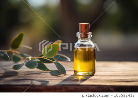 Eucalyptus Essential Oil in a small transparent glass bottle next to Eucalyptus Leaves on wooden surface with outdoor background. 105582432