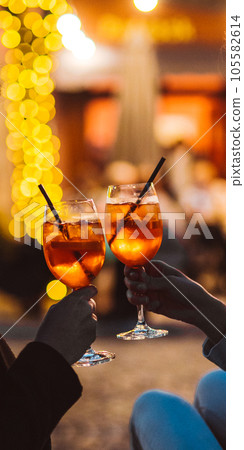 Vertical view of the hands of unknown woman and man clinking, cheers with glasses of Spritz cocktail 105582614