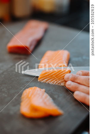 Vertical view of the hands of unknown man chief holding knife and cuts the salmon on wooden board 105582619