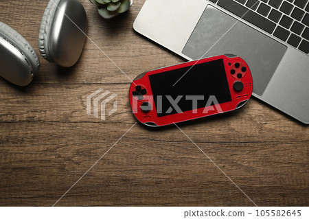 A video game console, laptop and wireless headphone on wooden table 105582645