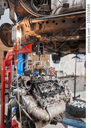A car mechanic inspects the engine with a flashlight. Engine Block on a repair stand with Special crane jack. Technical service station for car. 105583069