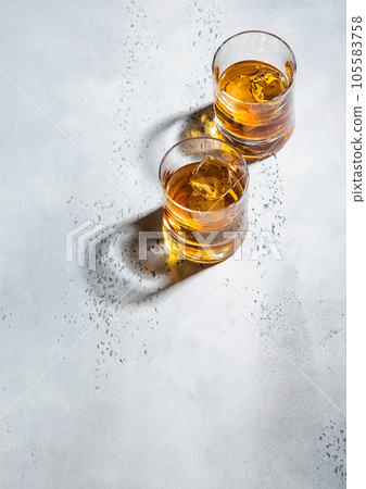 Two whiskey glasses with ice cubes on light background.Top view Two whiskey glasses with ice cubes on light background.Top view 105583758