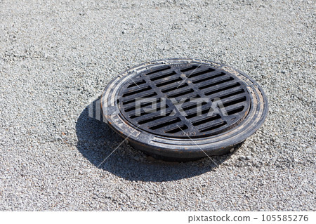 cast iron manhole on limestone pebbles top view on the road. Street Manhole Pavement cast iron manhole on limestone pebbles top view on the road. Street Manhole Pavement 105585276