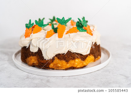 Decorating freshly baked carrot bundt cake with cream cheese frosting with chocolate carrot cake toppers. 105585443