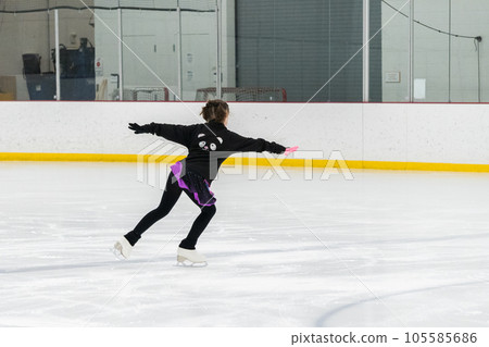 Young girl perfecting her figure skating routine while wearing her competition dress at an indoor ice rink. Young girl perfecting her figure skating routine while wearing her competition dress at an indoor ice rink. 105585686