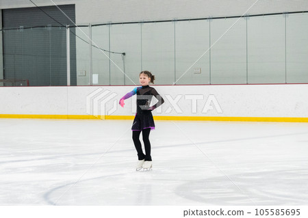 Young girl perfecting her figure skating routine while wearing her competition dress at an indoor ice rink. 105585695