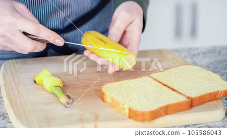 In a modern white kitchen, buttered banana and brioche bread are being prepared for making a delicious grilled peanut butter banana sandwich. 105586043