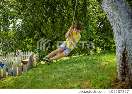 Happy little boy is having fun on a rope swing which he has found while having rest outside city. Active leisure time with children 105587237