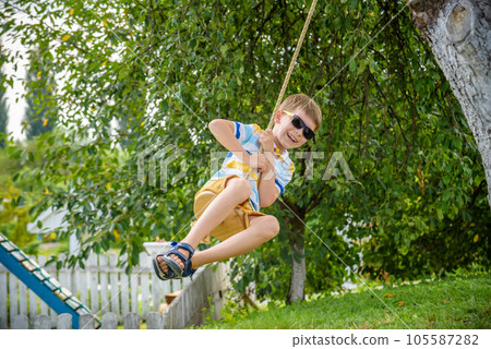 Happy little boy is having fun on a rope swing which he has found while having rest outside city. Active leisure time with children 105587282
