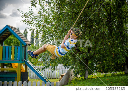 Happy little boy is having fun on a rope swing which he has found while having rest outside city. Active leisure time with children 105587285