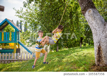 Two adorable happy little boys is having fun on a rope swing which he has found while having rest outside city. Active leisure time with children 105587356