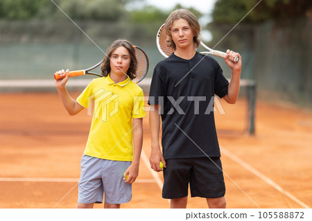 Two boys standing on the tennis court holding raquets 105588872