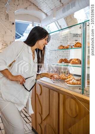 Woman observes cakes in coffee house display. Woman observes cakes in coffee house display. 105589658