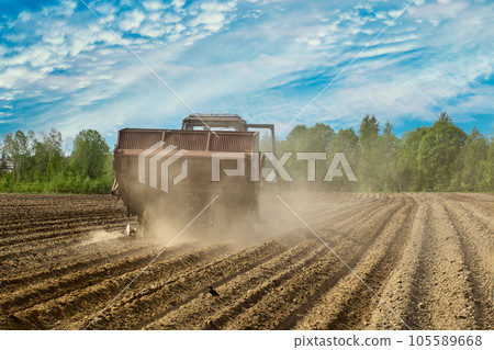 Potato planter in agricultural field raises cloud of dust in dry spring during sowing field work. 105589668
