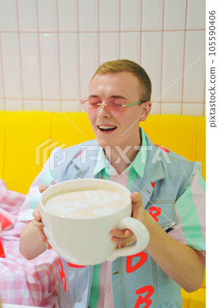 Young man in Ken doll costume Barbie friend in a cafe with a big cup of coffee Young man in Ken doll costume Barbie friend in a cafe with a big cup of coffee 105590406