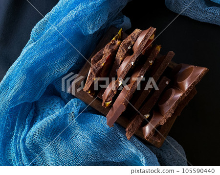 Pieces of chocolate with nuts and raisins on a dark background Pieces of chocolate with nuts and raisins on a dark background 105590440