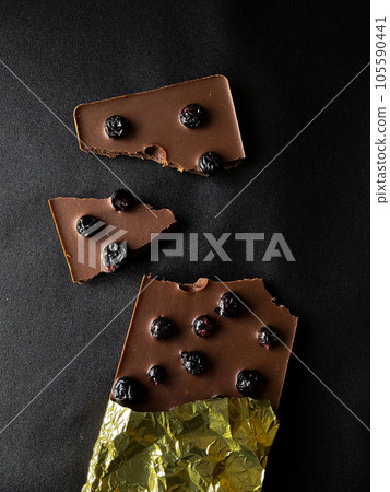 Dark chocolate broken with blueberries on a black background. View from above. Dark chocolate broken with blueberries on a black background. View from above. 105590441