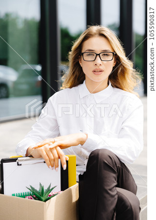 Caucasian businesswoman walking outdoors with box of stuff leaving business. Female office worker lost her job. Fired woman coming back home 105590817