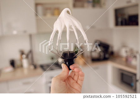 White cream mixer whisk in the hands of the girl in the kitchen. High quality photo 105592521