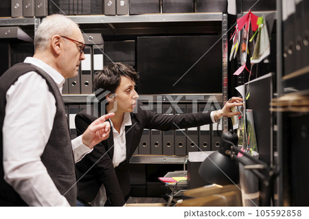 Investigators analyzing board with crime scene evidence, working late at night at criminal case in arhive room. Private detectives checking confidential files, discussing mysterious suspect report Investigators analyzing board with crime scene evidence, working late at night at criminal case in arhive room. Private detectives checking confidential files, discussing mysterious suspect report 105592858