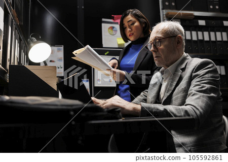 Business employees brainstorming accountancy data analysis report using laptop and statistics document records. Archive file room filled with cabinet, folders and flowcharts Business employees brainstorming accountancy data analysis report using laptop and statistics document records. Archive file room filled with cabinet, folders and flowcharts 105592861