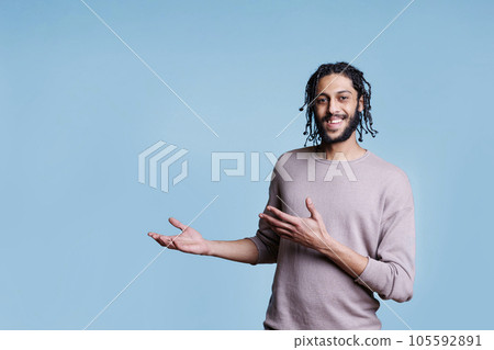 Cheerful arab man pointing with hands to right side while looking at camera. Smiling arabian person with joyful facial expression advertising product and showing with arms portrait 105592891
