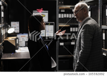 Accountancy asian assistant reporting budget plan optimizations to elderly businessman executive manager. Dark file cabinet office room surrounded by document folders on cabinet shelves Accountancy asian assistant reporting budget plan optimizations to elderly businessman executive manager. Dark file cabinet office room surrounded by document folders on cabinet shelves 105592892