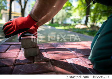 A skilled construction worker lays red paving stones on a sidewalk. 105593294