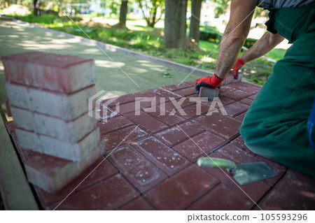 An experienced paving worker kneels while laying paving stones. An experienced paving worker kneels while laying paving stones. 105593296