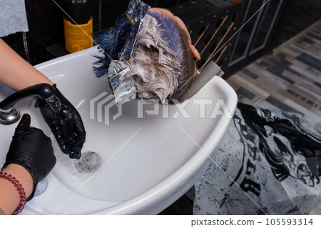 Washing the client's hair in the process of coloring the client's stylish coloring at work, in a barbershop or service salon 105593314