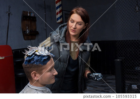 Brunette adult girl caucasian worker portrait salon in the process of color stylish fashion hair coloring for a young client guy Brunette adult girl caucasian worker portrait salon in the process of color stylish fashion hair coloring for a young client guy 105593315