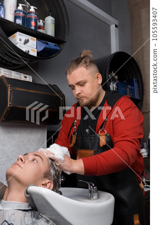 A man in a normal mood, a European handsome barber, a professional washes the head of a client, a young handsome guy, a Caucasian with foam over the sink before a haircut 105593407