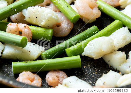 A cooking scene where seafood (squid and shrimp) and garlic sprouts are fried in a frying pan. 105599583