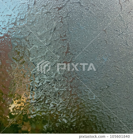 Frozen glass with the onset of cold weather. View through a layer of ice to the blue sky. Frost on the windshield, the rays of the morning sun melt the frost formed overnight. Background, texture. Frozen glass with the onset of cold weather. View through a layer of ice to the blue sky. Frost on the windshield, the rays of the morning sun melt the frost formed overnight. Background, texture. 105601840