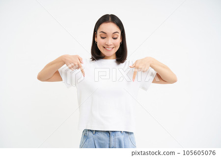 Portrait of beautiful smiling korean girl, points fingers down, shows advertisement, demonstrates banner below, isolated on white background 105605076