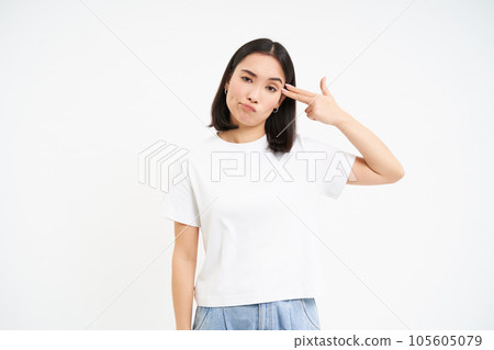 Annoyed asian woman, student shows finger pistol near head, looks bothered and tired, stands isolated on white background 105605079