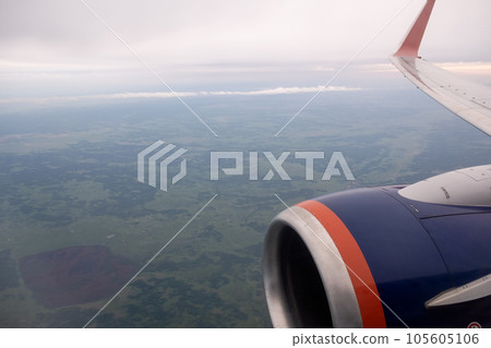 Airplane flight. Wing of an airplane flying above the clouds. View from the window of the plane. Airplane, Aircraft. Traveling by air. Aircraft's wing and land seen through the illuminator. Airplane flight. Wing of an airplane flying above the clouds. View from the window of the plane. Airplane, Aircraft. Traveling by air. Aircraft's wing and land seen through the illuminator. 105605106