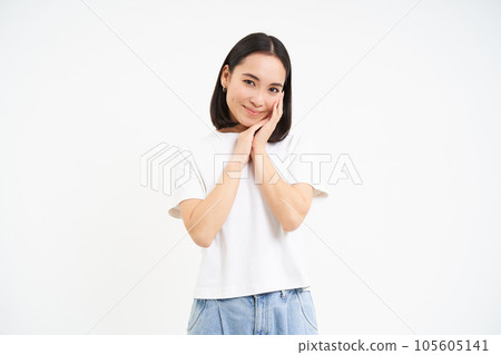 Portrait of tender, cute young asian woman, looking with flirty, silly ace expression, standing over white background 105605141