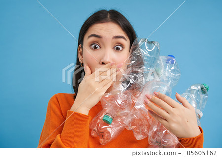 Surprised korean woman, holding plastic bottles, looking shocked at camera, concept of environment and recycling, blue background Surprised korean woman, holding plastic bottles, looking shocked at camera, concept of environment and recycling, blue background 105605162