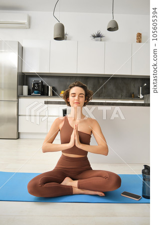 Vertical shot of young woman meditating, doing yoga at home on rubber mat at home 105605394