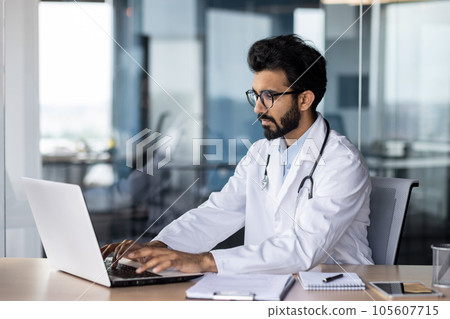 Concentrated and serious indian male doctor student studying online in office at laptop. 105607715