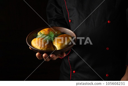 The chef holds in his hand a plate with freshly baked pies or dill buns. Free black space for menu or recipe 105608231