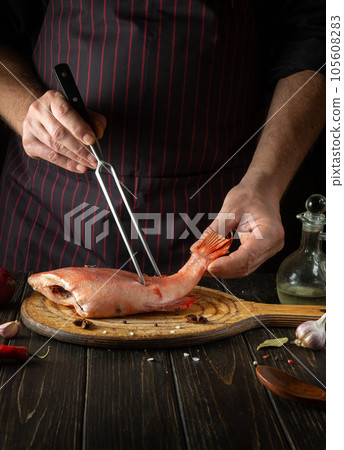The cook prepares fish Sebastes in the hotel kitchen. The concept of cooking fish on a dark background. European cuisine The cook prepares fish Sebastes in the hotel kitchen. The concept of cooking fish on a dark background. European cuisine 105608283
