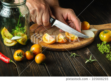 Preparation of canned vegetable salad. Chef hands cut tomatoes on a cutting board with a knife. Peasant food 105608293