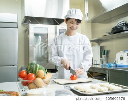 Young woman in cooking clothes cutting tomatoes in the kitchen 105609676