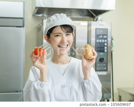 Young woman in cooking clothes standing in the kitchen and holding tomatoes and potatoes Young woman in cooking clothes standing in the kitchen and holding tomatoes and potatoes 105609697