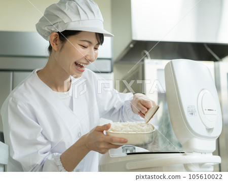 Young woman in cooking clothes serving rice from the rice cooker in the kitchen 105610022