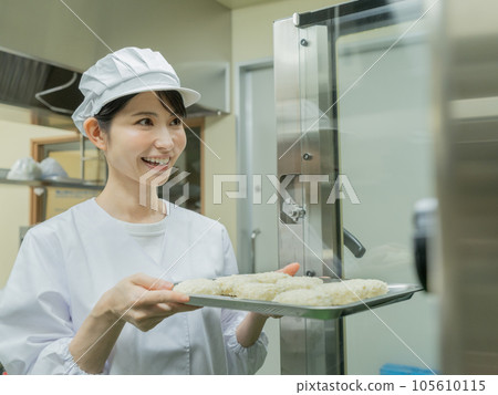 穿著做飯服的年輕女子將炸丸子放入廚房的烤箱中 穿著做飯服的年輕女子將炸丸子放入廚房的烤箱中 105610115