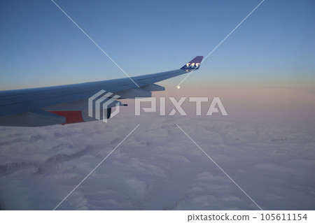 KOPENHAGEN, DENMARK - 24 NOV 2018: View from the aircraft cabin to the wing at sunset over the icebergs of Greenland KOPENHAGEN, DENMARK - 24 NOV 2018: View from the aircraft cabin to the wing at sunset over the icebergs of Greenland 105611154