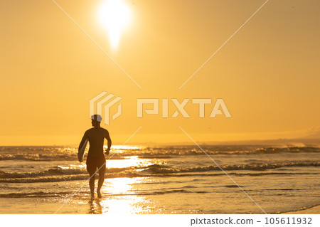 Silhouette of a man surfer walking to the ocean at bright sunset 105611932